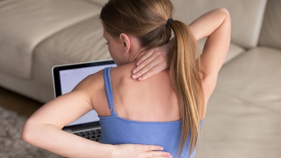 woman experiencing back and shoulder pain while working on a laptop